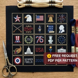 May include: A black cross-stitch fabric featuring a grid of 25 patriotic American icons, including an eagle, the Liberty Bell, the Statue of Liberty, and the text 250th, USA, and 2026. Includes two embroidery floss skeins and vintage-style scissors.