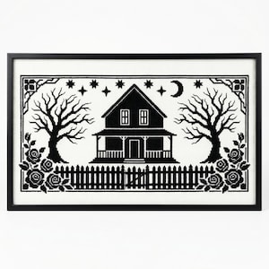 May include: Framed black and white cross-stitch art featuring a house, trees, and a fence. The design includes stars, a crescent moon, and floral accents. The artwork is displayed in a black frame.
