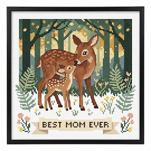 May include: Cross-stitch artwork in a black frame depicts a mother deer and fawn in a forest setting. The mother deer is brown, and the fawn is spotted. The background features trees and the text "BEST MOM EVER" on a banner.