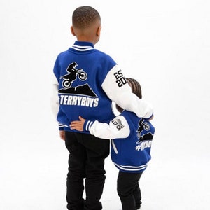 Pode incluir: Dois meninos jovens vestindo jaquetas de beisebol azul e branco com um design de motocross nas costas. As jaquetas t&ecirc;m o texto "#TERRYBOYS" e "#WYB" nas costas.