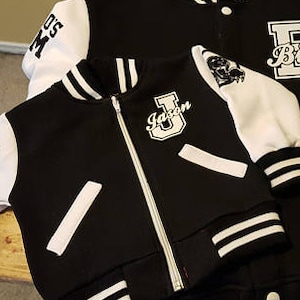 May include: Two black and white varsity jackets with white sleeves. The larger jacket has the word "Bird" on the front. The smaller jacket has the word "Jason" on the front.