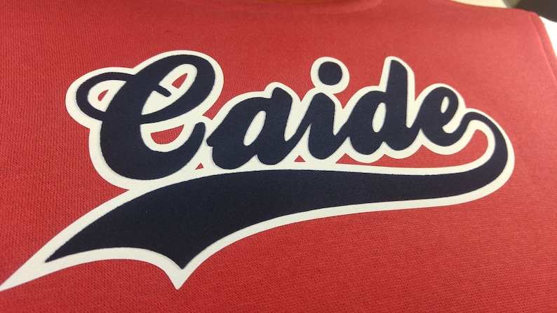 Może przedstawiać: Czerwona bluza z białym obramowaniem i granatowym napisem "Caide" w ozdobnym, pisanym stylu.