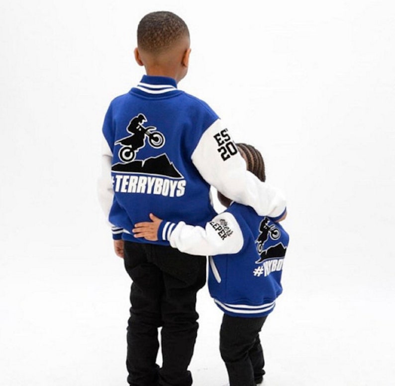 Pode incluir: Dois meninos jovens vestindo jaquetas de beisebol azul e branco com um design de motocross nas costas. As jaquetas t&ecirc;m o texto "#TERRYBOYS" e "#WYB" nas costas.