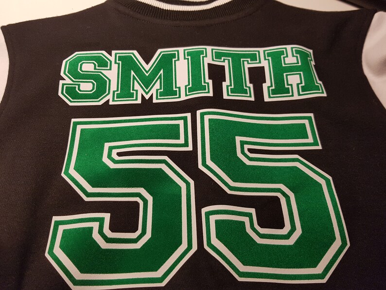 Może przedstawiać: Czarna i zielona kurtka bejsbolowa z nazwiskiem "SMITH" i numerem "55" na plecach.