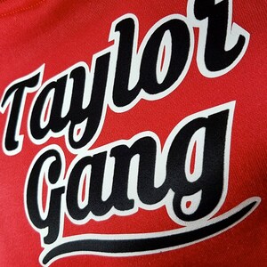Pode incluir: Camisola vermelha com texto preto que l&ecirc; "Taylor Gang" em um tipo de letra estilizado.