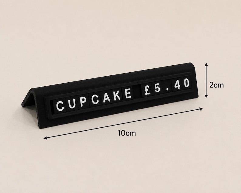 May include: A black L-shaped price tag stand featuring white letter tiles that spell out CUPCAKE &pound; 5.40. The stand measures 10 cm in length and 2 cm in height as indicated by the black dimension arrows printed on the image.