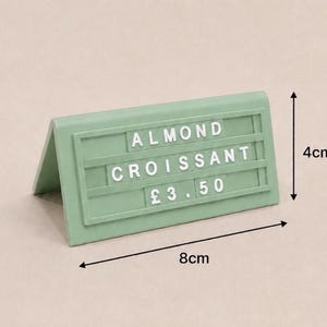 May include: A sage green tent-style sign with white plastic letters spelling ALMOND CROISSANT and the price &pound;3.50. The sign measures 4 cm in height and 8 cm in width, featuring three horizontal rows for interchangeable characters on its front face.