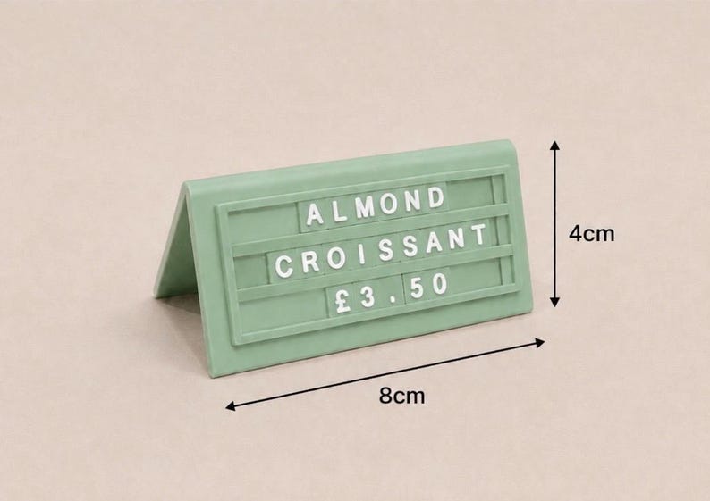 May include: A sage green tent-style sign with white plastic letters spelling ALMOND CROISSANT and the price &pound;3.50. The sign measures 4 cm in height and 8 cm in width, featuring three horizontal rows for interchangeable characters on its front face.