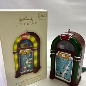 May include: A Hallmark Keepsake Christmas ornament shaped like a vintage jukebox. The ornament is brown with green and red accents, and features a blue and silver design on the front. The box reads "Swingin' Into Christmas".