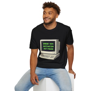 Può includere: T-shirt nero con grafica di computer retrò. Il design presenta un monitor e una tastiera di computer vintage, con la scritta verde "ERROR 404: MOTIVATION NOT FOUND". Un design umoristico a tema tecnologico.