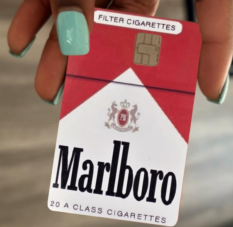 May include: A rectangular credit card skin featuring a red and white design modeled after a pack of Marlboro cigarettes. The card displays the text FILTER CIGARETTES, the Marlboro logo, and the text 20 A CLASS CIGARETTES with a gold EMV chip.