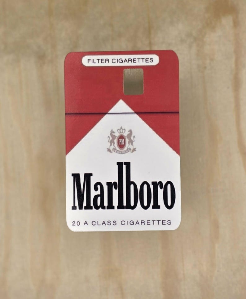 May include: A rectangular Marlboro cigarette pack featuring a red and white design. The top section is red with the text FILTER CIGARETTES. The white lower section displays the Marlboro logo, a crest, and the text 20 A CLASS CIGARETTES.