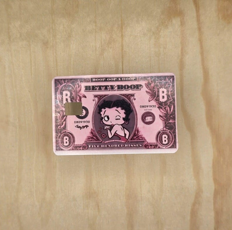 May include: A rectangular pink sticker designed to look like a banknote featuring Betty Boop. The text reads Boop Oop A Doop, Betty Boop, 08091930, and Five Hundred Kisses. It includes a square cutout on the left side and the letter B in corners.