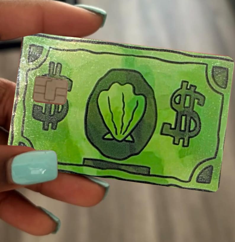 May include: A rectangular credit card skin featuring a bright green color scheme with a hand-drawn aesthetic. The design includes a central dark green circle containing a light green seashell illustration, flanked by black dollar signs and a chip.