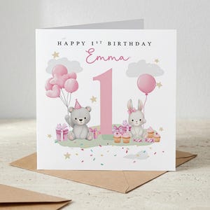 May include: A birthday card with the text "Happy 1st Birthday Emma". The card features a pink number one, a teddy bear with balloons, and a bunny with a balloon. Pink gifts, cupcakes, and confetti complete the design.