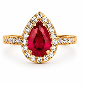 Op de afbeelding: Een gouden ring met een grote peervormige rode edelsteen in het midden, omringd door een halo van kleine heldere ronde stenen. De ringband is aan beide zijden ook bezet met een rij kleine heldere ronde stenen voor een glanzende uitstraling.