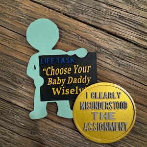 Puede incluir: Una figura de color verde claro sosteniendo un letrero negro con el texto "LIFE TASK: Choose Your Baby Daddy Wisely" en amarillo y blanco. Una moneda de oro con el texto "I CLEARLY MISUNDERSTOOD THE ASSIGNMENT" está junto a la figura.