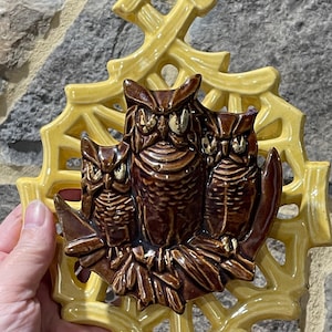 May include: A ceramic owl wall hanging featuring three brown owls perched on a branch, set against a yellow, openwork background. The owls have detailed features and golden accents. The piece is likely vintage and decorative.