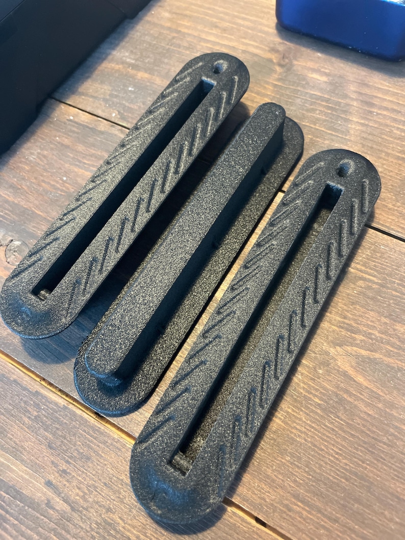 Three matte black 3D-printed Single-Tab fin boxes for Thruster setups, compatible with Futures fin systems, made from carbon fiber reinforced nylon on a wooden background.