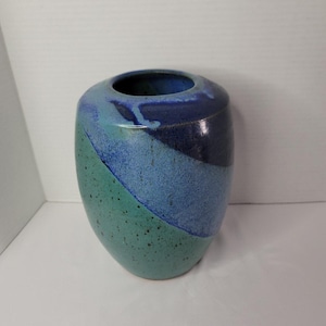 Könnte beinhalten: Eine Keramikvase mit abgerundeter Form und breiter Öffnung. Die Vase hat ein diagonales Farbblockdesign in Blau- und Türkistönen mit einer gesprenkelten Textur. Der Innenraum ist tiefblau.
