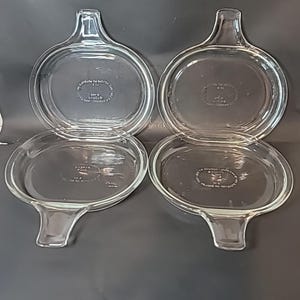 Może przedstawiać: Cztery przezroczyste szklane pokrywki Pyrex z uchwytem. Pokrywki mają owalny kształt z zaokrąglonym uchwytem z jednej strony. Szkło jest przezroczyste, a pokrywki wydają się być w dobrym stanie. Pokrywki są do naczyń kuchennych.