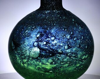 May include: A spherical glass vase featuring a gradient colour transition from deep blue at the top to vibrant green at the base. The surface is textured with numerous small air bubbles and a dark, speckled pattern throughout the glass body.