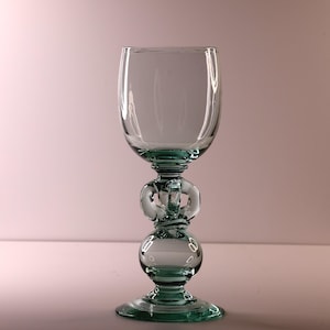 May include: A clear glass goblet with a teal base and stem. The stem has rounded, decorative features. The bowl is a classic rounded shape. The goblet is designed for beverages.