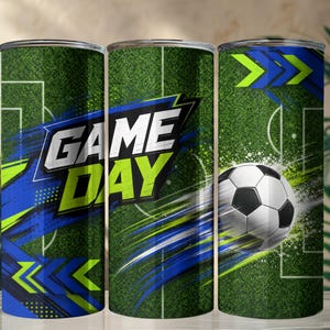 Può includere: Un bicchiere cilindrico con un motivo a campo da calcio verde e linee bianche. Il design include un pallone da calcio bianco e nero, pennellate astratte blu e verde lime e la scritta GAME DAY in grassetto bianco.