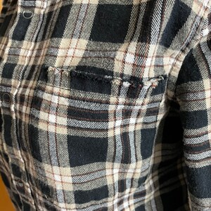 May include: A black and white plaid flannel shirt with brown accents. The shirt has a pocket on the left side and a frayed edge.