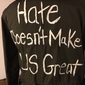 May include: A green hooded jacket with the phrase "Hate Doesn't Make Us Great" written in white paint on the back.