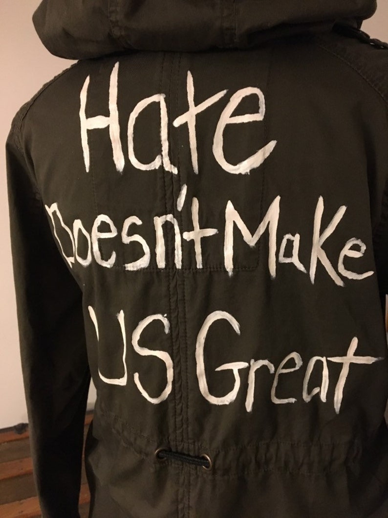 May include: A green hooded jacket with the phrase "Hate Doesn't Make Us Great" written in white paint on the back.