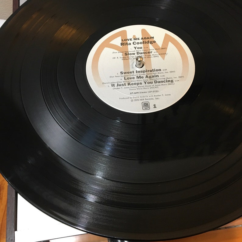 May include: A black vinyl record with a white label. The label features the text "Love Me Again" by Rita Coolidge. The record is labeled "SP-4479/Stereo (SP-5135)" and is produced by Dan Addis with Booker T. Jones. The record is from A&M Records, Inc.