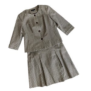 Puede incluir: Un traje de dos piezas para mujer con chaqueta y falda. La chaqueta tiene mangas tres cuartos y cierre de botones. La falda es plisada. Ambas piezas están estampadas con un diseño geométrico repetitivo en tonos marrones y blancos.