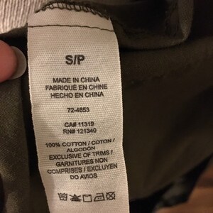May include: White clothing tag with black text. The tag says "S/P", "Made in China", "Fabriqu&eacute; en Chine", "Hecho en China", "72-4653", "CA# 11319", "RN# 121340", "100% Cotton/Coton/Algod&oacute;n", "Exclusive of Trims/Garnitures Non Comprises/Excluyen Do Avio", and has care instructions.