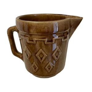 May include: A brown ceramic pitcher with a diamond pattern and a handle. The pitcher has a brown glaze and a slightly textured surface.
