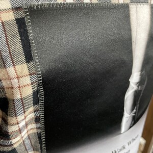 May include: A black and white image of a ballerina's leg in a pointe shoe. The image is sewn onto a brown and white plaid fabric. The text "Why Walk When You Can Dance" is printed below the image.