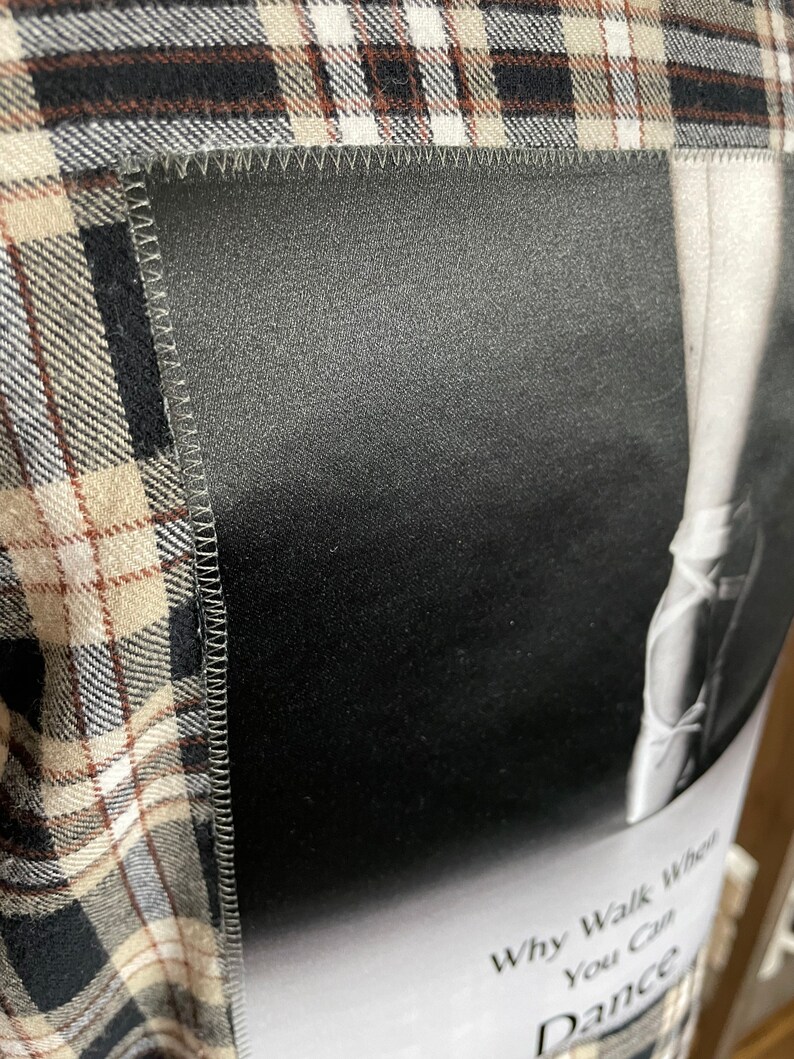 May include: A black and white image of a ballerina's leg in a pointe shoe. The image is sewn onto a brown and white plaid fabric. The text "Why Walk When You Can Dance" is printed below the image.