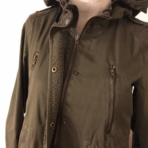 May include: A green hooded jacket with a zipper closure and multiple pockets. The jacket has a button closure at the neck and a drawstring hood.