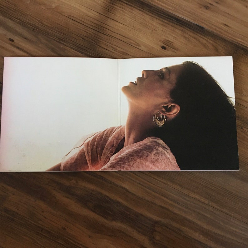May include: A woman with long dark hair is wearing a pink and white dress. She is looking up and her head is tilted back. She is wearing gold hoop earrings.