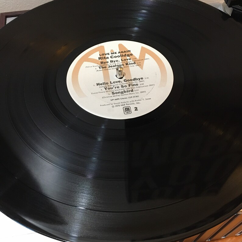 May include: A black vinyl record with a white label. The label has the text "LOVE ME AGAIN Rita Coolidge" and lists the songs "Bye Bye, Love", "The Jealous Kind", "Hello Love, Goodbye", "You're So Fine", and "Songbird".