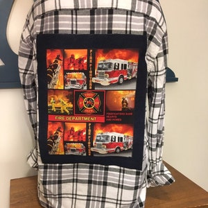 May include: A black and white plaid flannel shirt with a blue patch on the back. The patch features a collage of images of firefighters, fire trucks, and the words "Fire Department" and "Firefighters save hearts and homes".