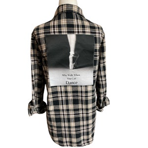 May include: Black and beige plaid flannel shirt with a large image of a ballerina's foot in a pointe shoe on the back. The image has the text "Why Walk When You Can Dance" underneath.