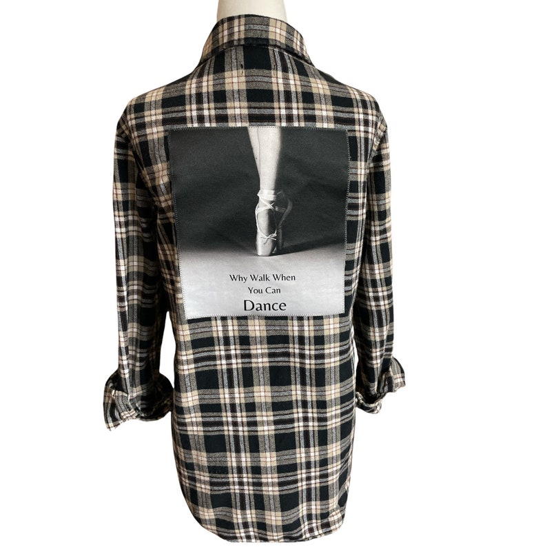 May include: Black and beige plaid flannel shirt with a large image of a ballerina's foot in a pointe shoe on the back. The image has the text "Why Walk When You Can Dance" underneath.