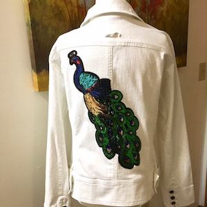 May include: White denim jacket with a sequined peacock design on the back.