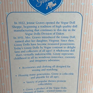 May include: A close-up of a box with the name "Ginny" in a blue heart-shaped logo. The box contains text about the Ginny doll, including its history, features, and collectible nature. The background is a light pink with a repeating heart pattern.