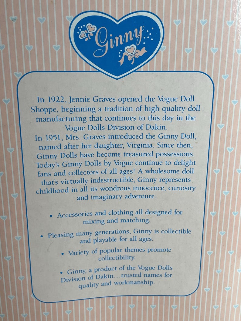 May include: A close-up of a box with the name "Ginny" in a blue heart-shaped logo. The box contains text about the Ginny doll, including its history, features, and collectible nature. The background is a light pink with a repeating heart pattern.