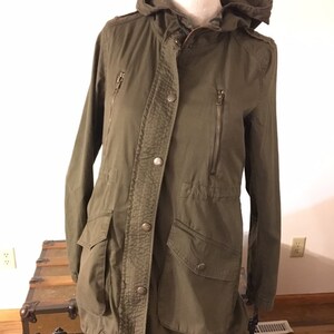 May include: A long-sleeved, olive green hooded jacket with a zipper and button closure. The jacket has two zippered pockets on the front and two flap pockets on the bottom.