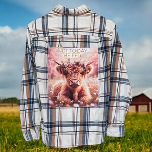 May include: Plaid button-down shirt with a graphic of a Highland cow wearing a flower crown. The graphic includes the text "NOT TODAY HEIFER". The shirt has a white, brown, and navy blue plaid pattern.