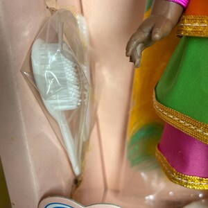 May include: A vintage Ginny doll in a pink box. The doll has a colorful dress with gold trim and a pink top. A white toothbrush is in a plastic bag. The Ginny label is visible.
