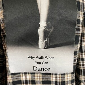 May include: A black and white photo of a ballerina's foot in a pointe shoe. The photo is on a black and white plaid fabric background. The text "Why Walk When You Can Dance" is printed below the photo.